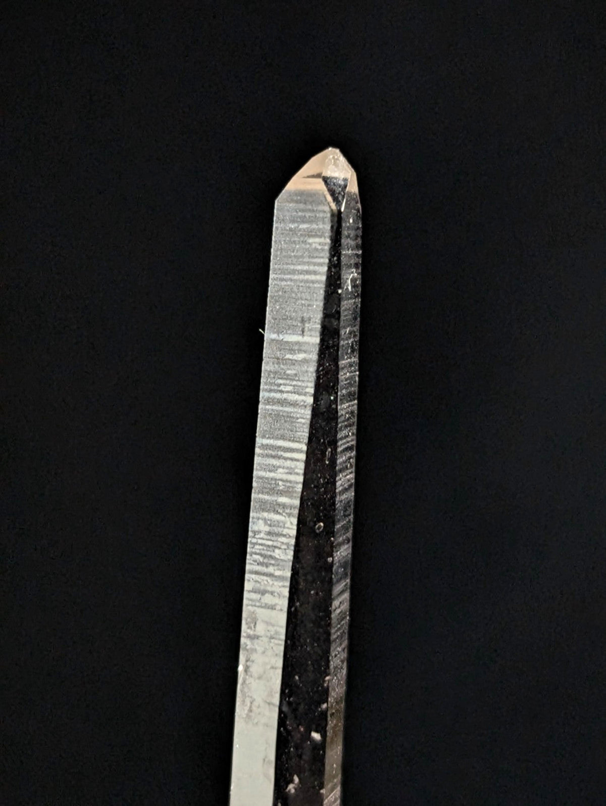 A clear quartz crystal with a pointed tip and visible striations along its length.