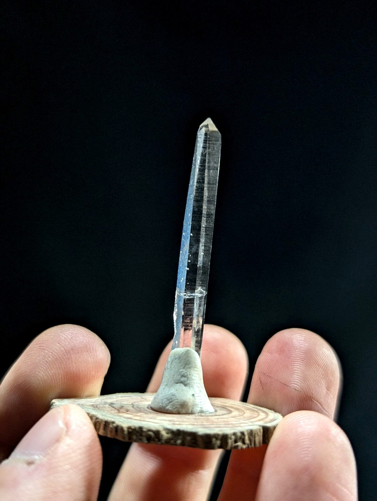 A clear quartz crystal with a pointed tip, mounted on a rustic wooden base.
