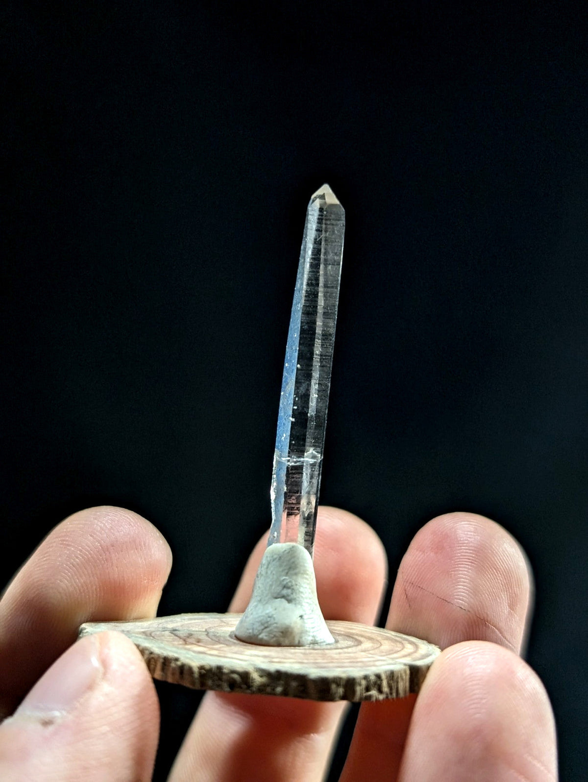 A clear quartz crystal with a pointed tip, mounted on a rustic wooden base.