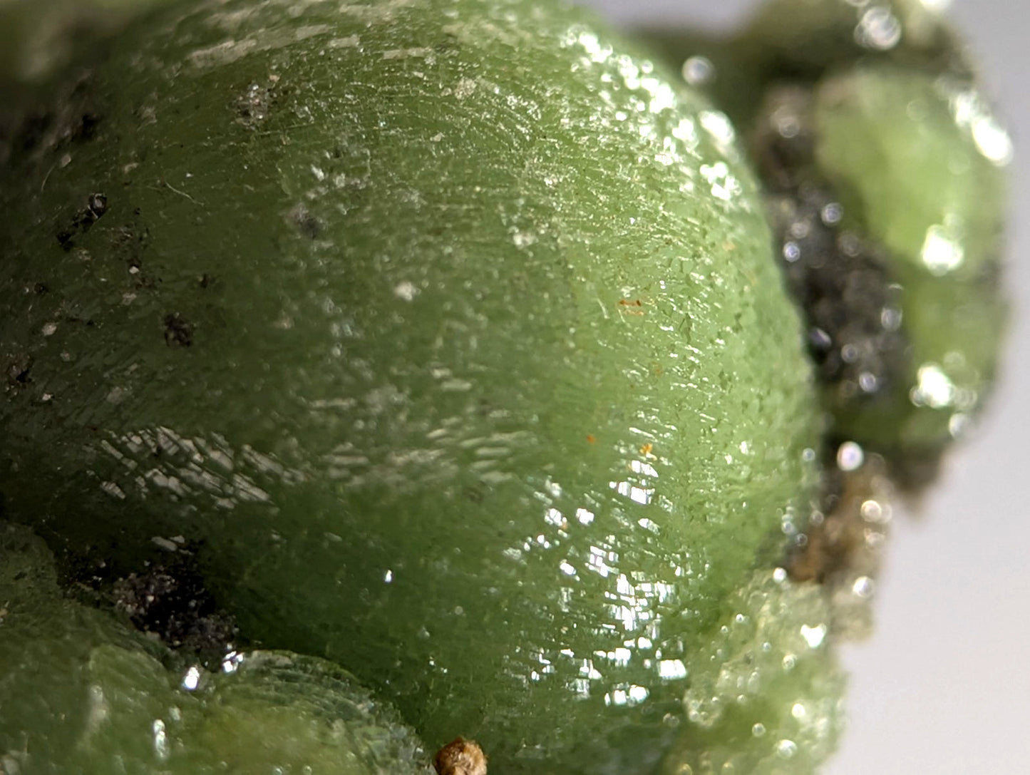 A glossy translucent green wavellite with textured surface and dark specks mounted on handmade wood from montgomery county arkansas