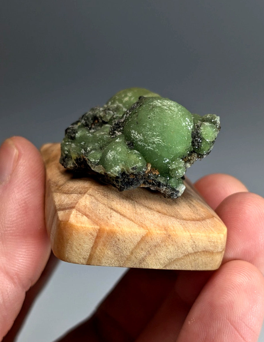 A vibrant green glossy wavellite mineral with rough clustered texture on a handmade wood mount from arkansas