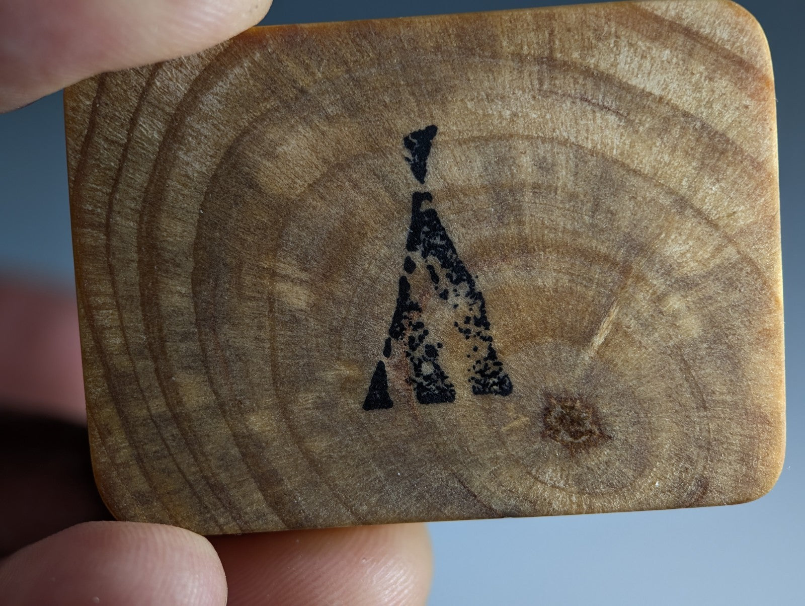 A rectangular wooden coaster with natural grain and black abstract giraffe stamp with handmade mount from montgomery county arkansas