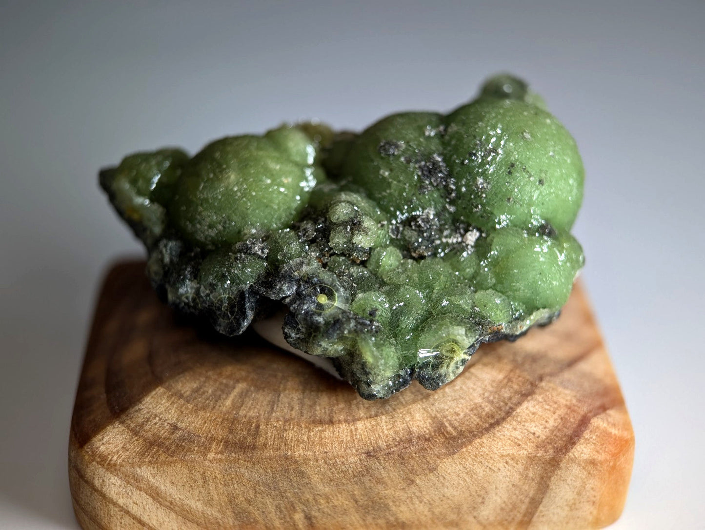 A vibrant green bumpy A+++ museum grade wavellite with dark speckles on a handmade wood mount from Arkansas