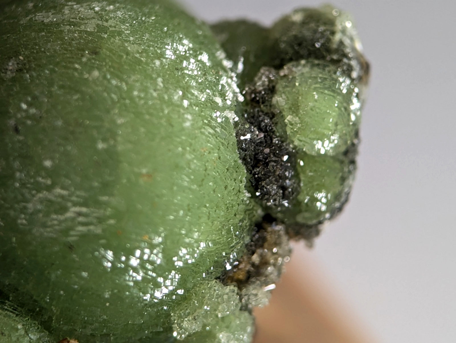A translucent green wavellite mineral with glossy crystalline surface and dark inclusions on handmade wood mount from montgomery county arkansas