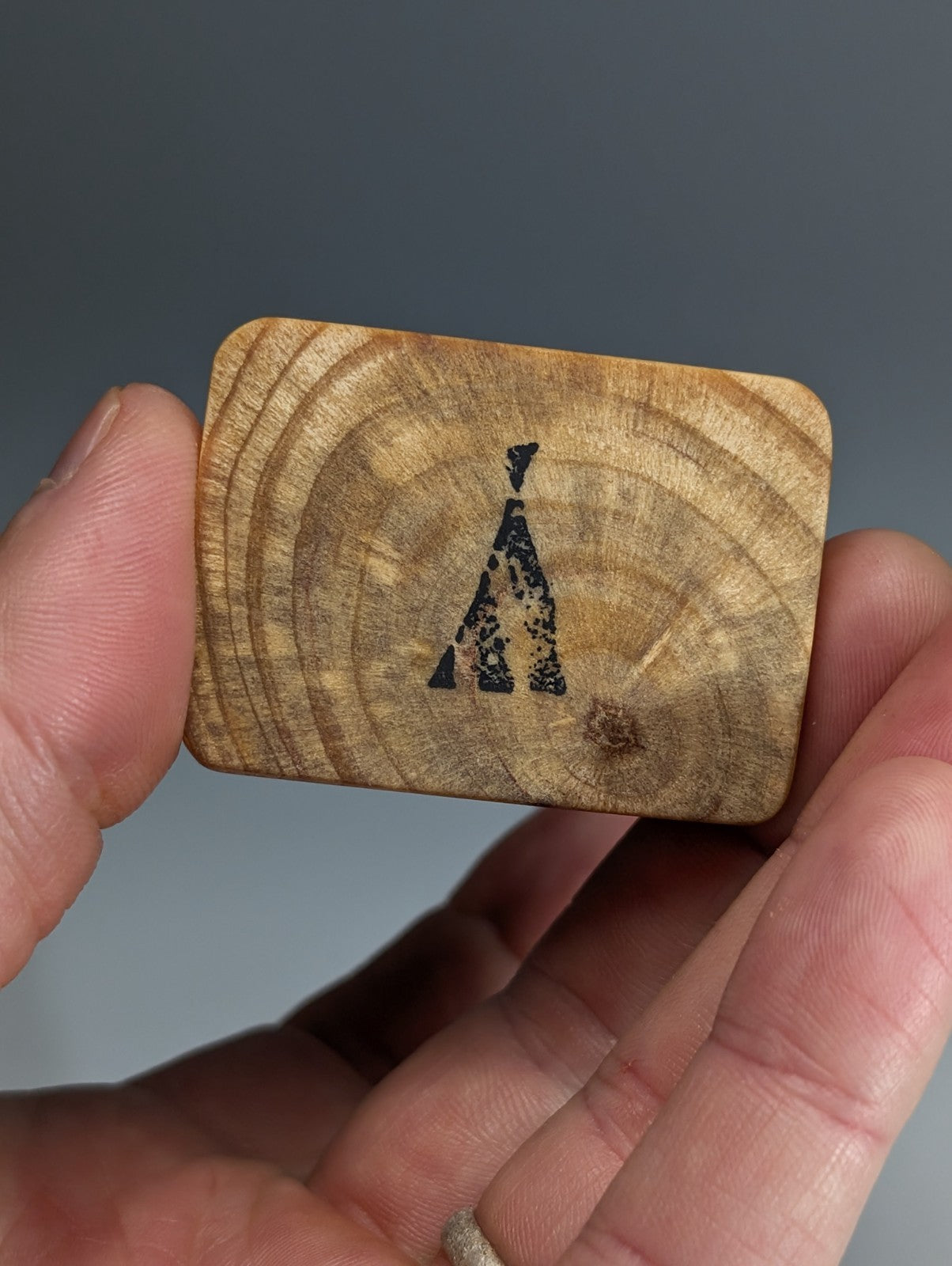 A rectangular wooden card with natural wood grain and black stenciled logo handmade wood mount for wavellite