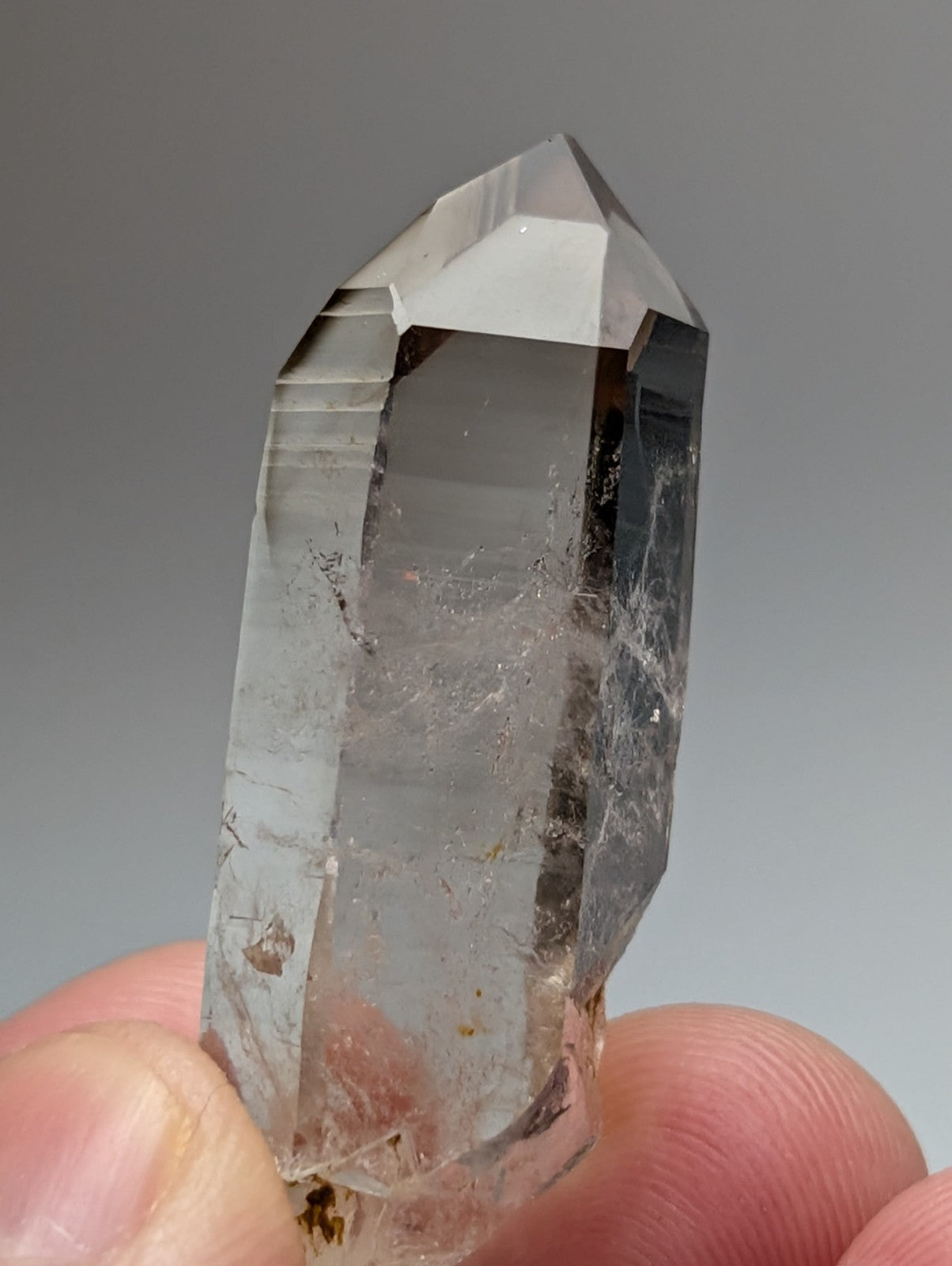 A clear quartz crystal point with visible inclusions held between fingers from Garland County Arkansas USA