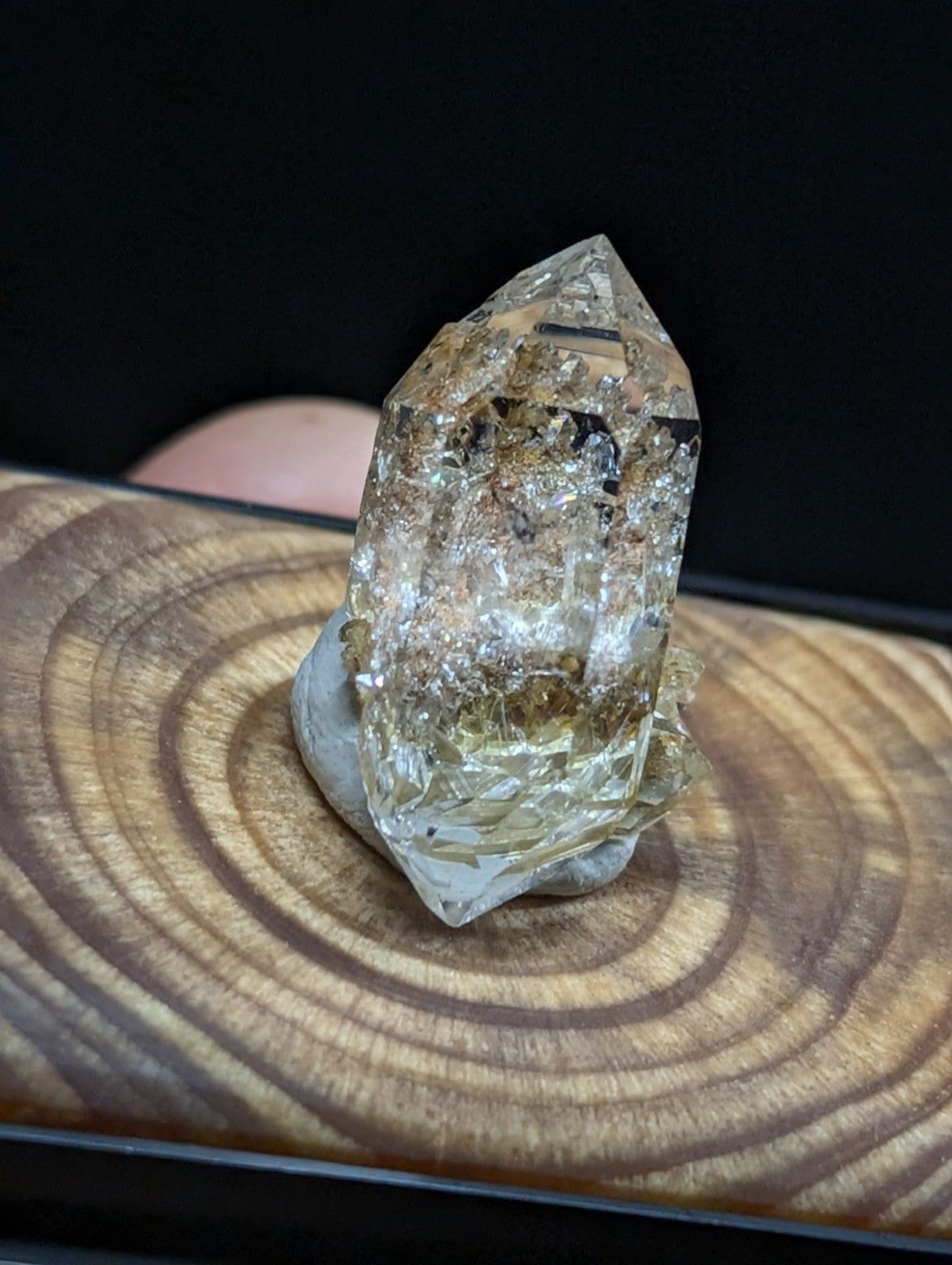 A translucent, golden-hued quartz crystal with natural inclusions and a pointed tip rests on a wooden base.
