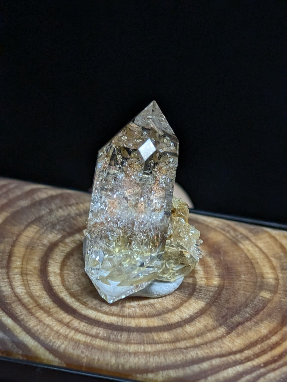 A translucent golden quartz crystal with a pointed top and embedded metallic inclusions, displayed on a wooden base.