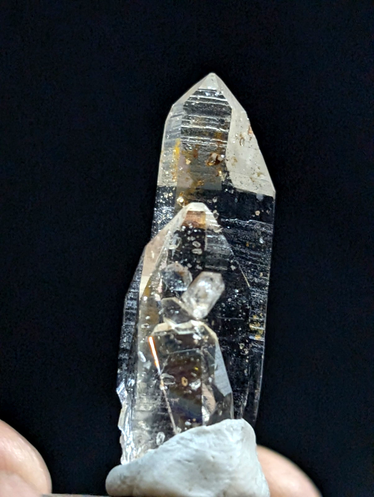 A clear quartz crystal with a pointed tip and internal inclusions, held upright against a dark background.