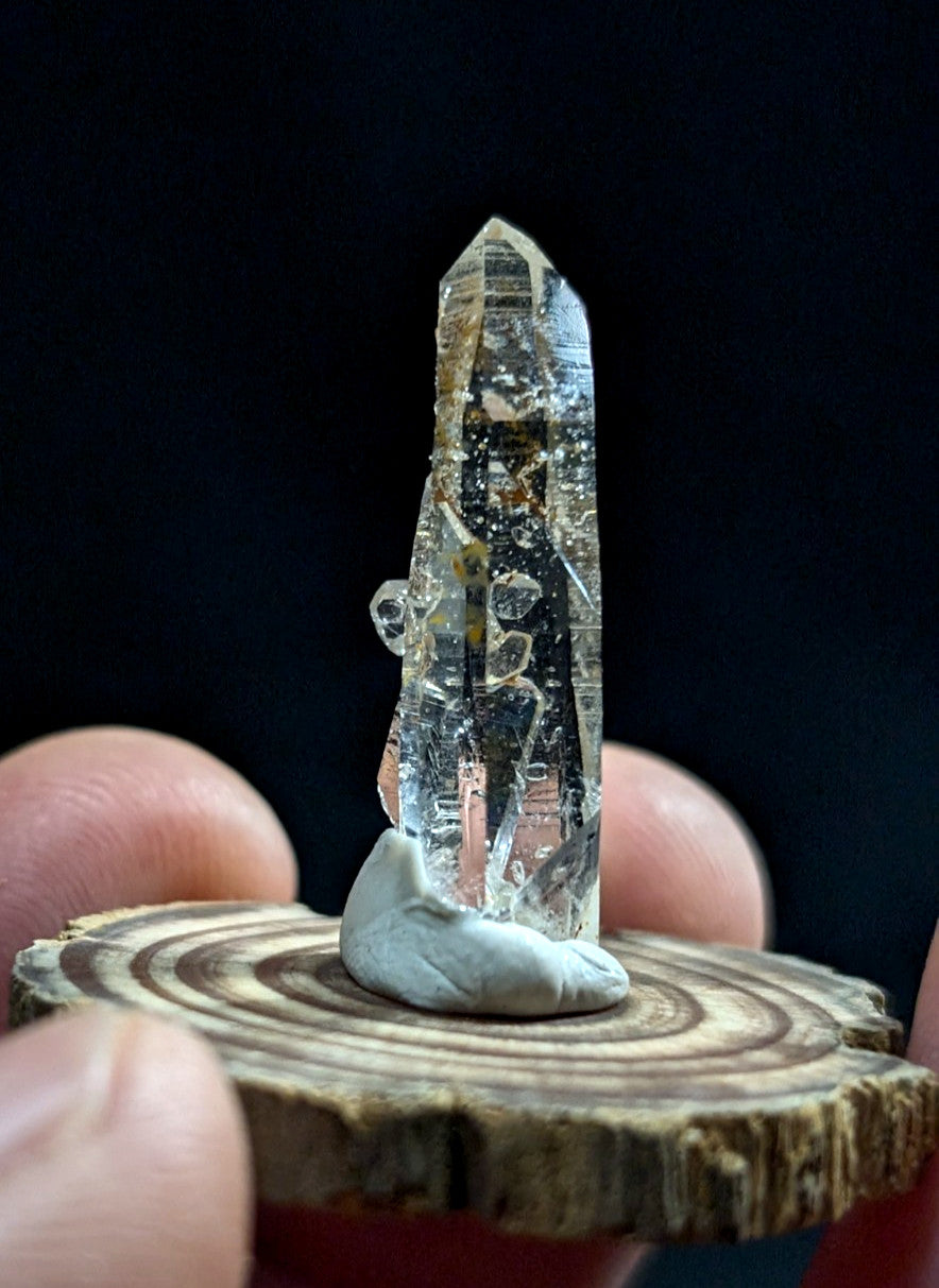 A clear quartz crystal with natural inclusions and a pointed tip, displayed on a small wooden slice base.
