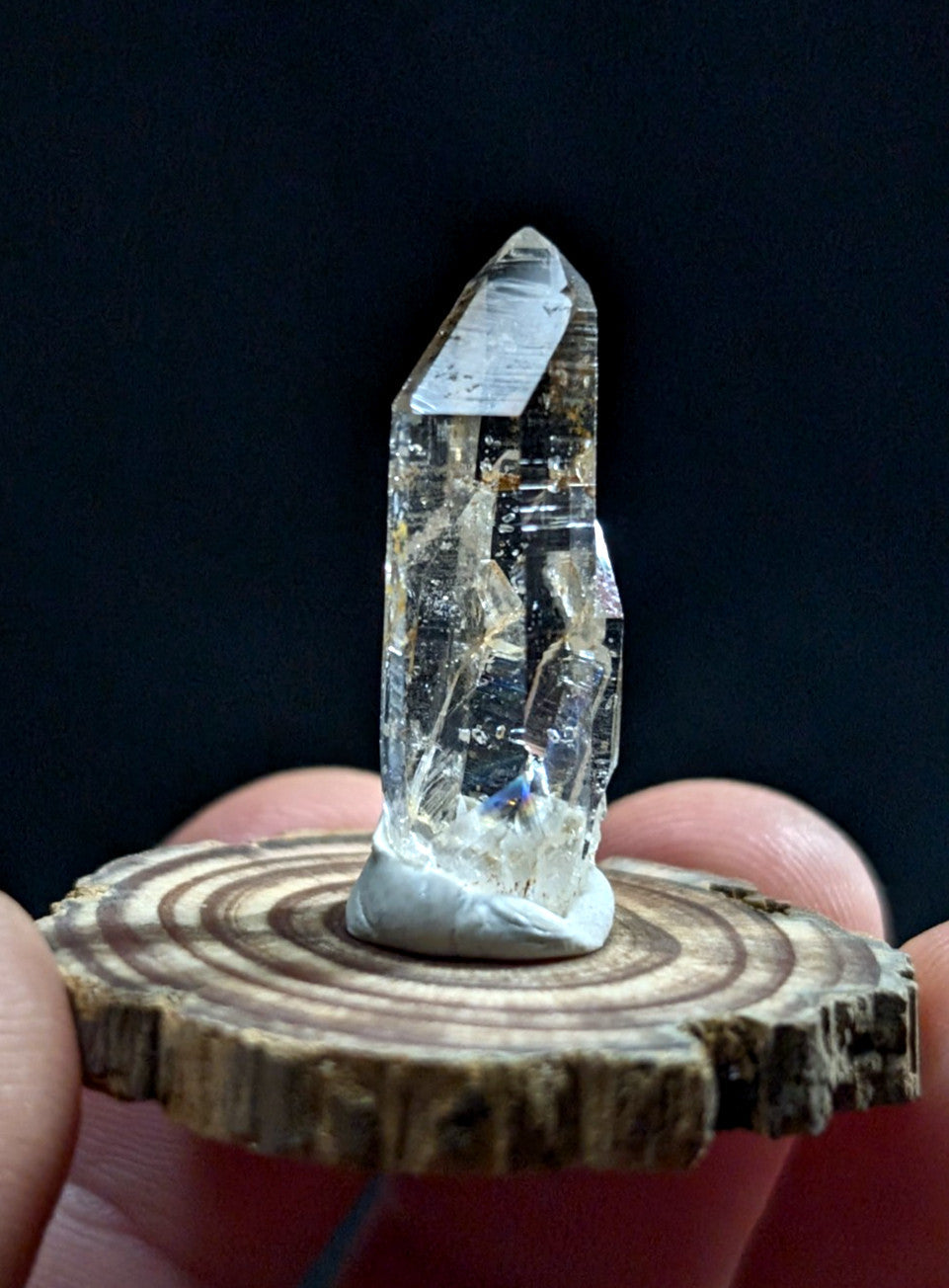 A clear, translucent quartz crystal with natural inclusions and a pointed tip sits upright on a circular wooden slice.