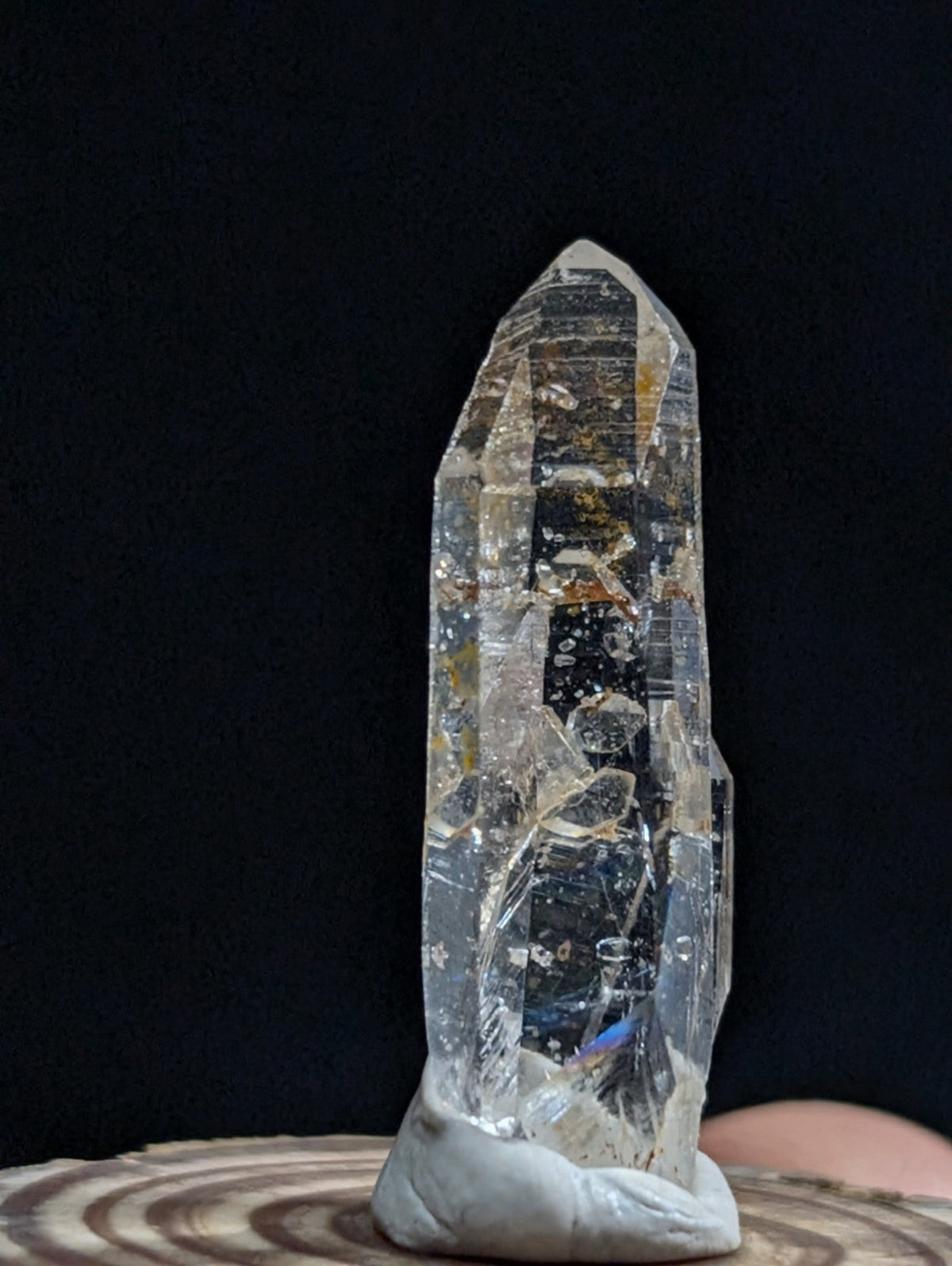 A tall, transparent quartz crystal with natural inclusions and a pointed tip, mounted on a light gray base.