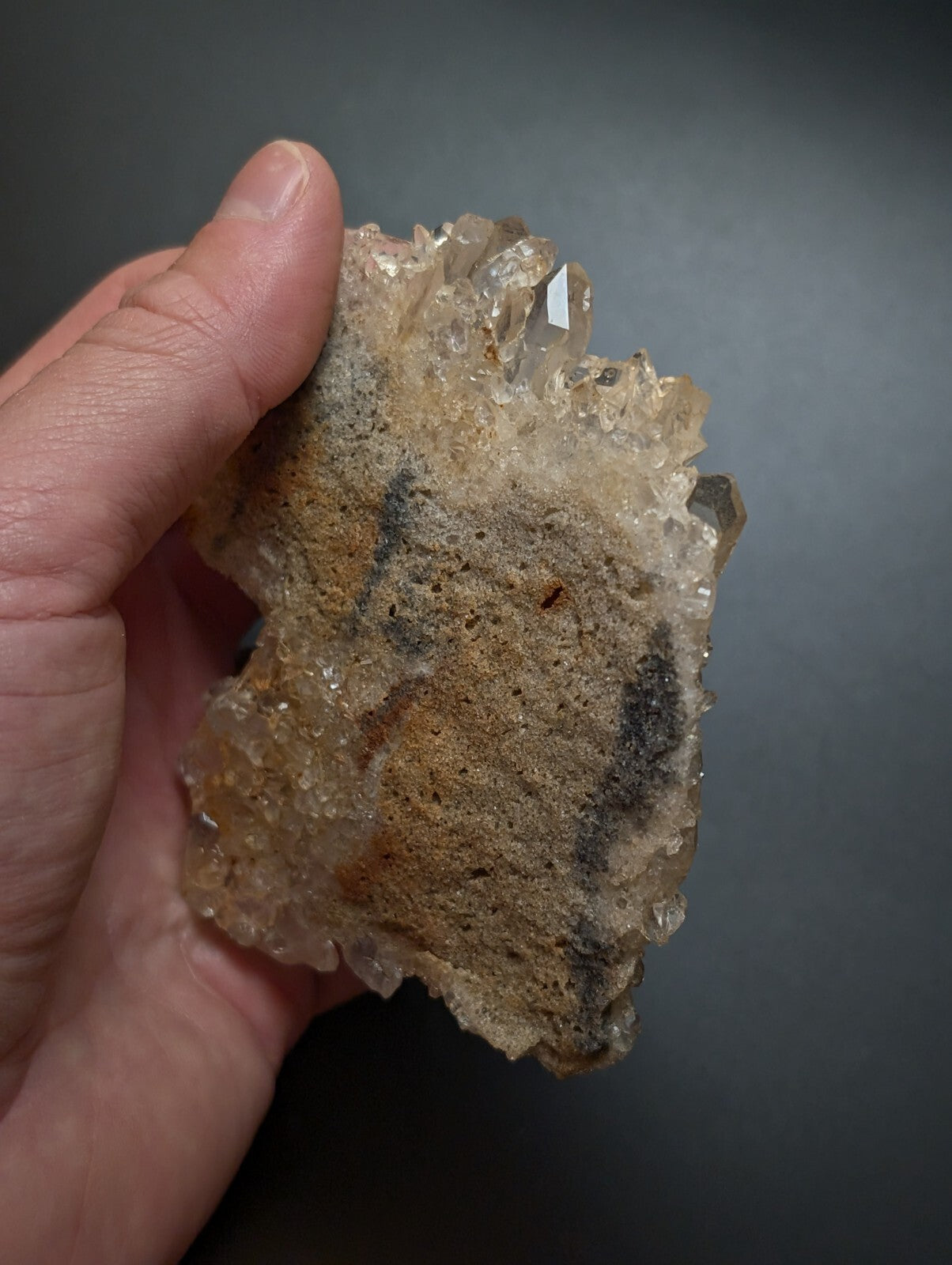 A hand holds a rough, translucent quartz crystal cluster with jagged edges and earthy brownish-yellow tones.