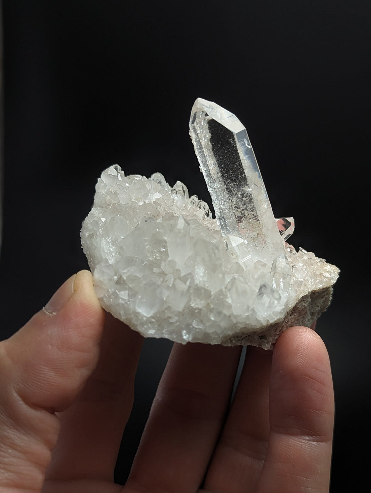A clear, translucent quartz crystal cluster with a prominent pointed spike rising from a dense mass of smaller crystals.