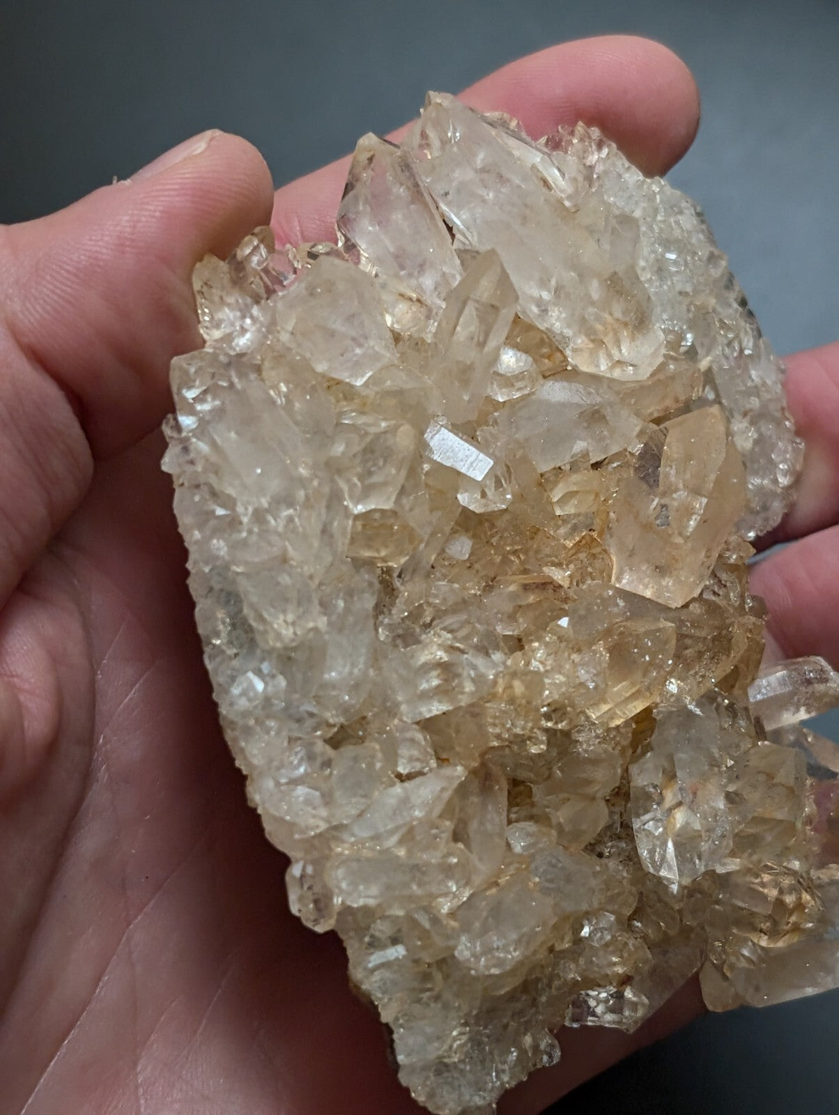 A cluster of translucent, pale yellowish quartz crystals held in a hand.