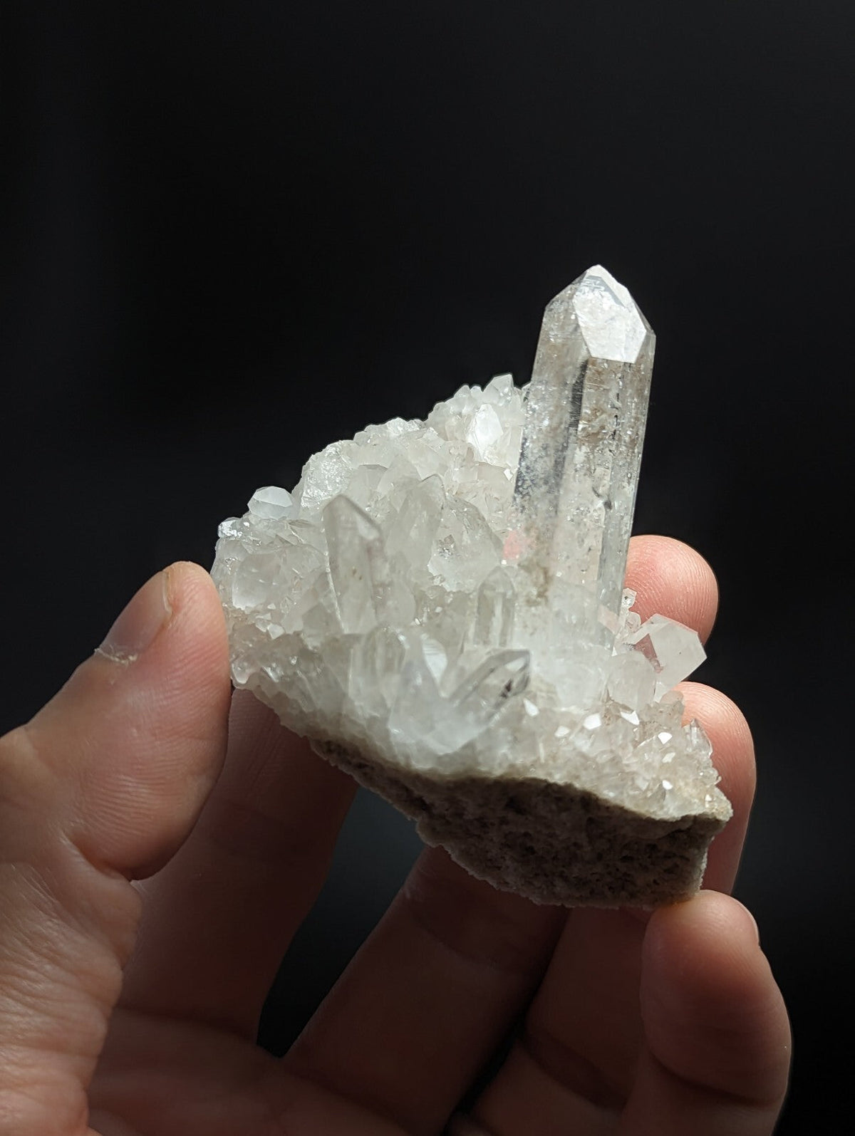 A translucent white quartz crystal cluster with a prominent tall, clear point emerging from a dense formation of smaller crystals.