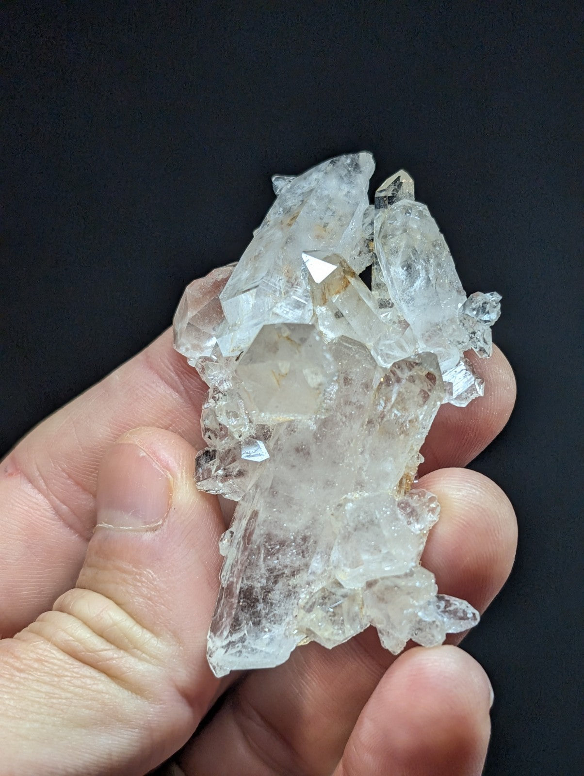 A cluster of clear, faceted quartz crystals held in a hand.