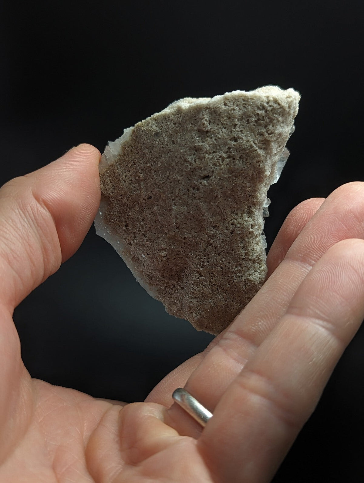 A rough, irregularly shaped piece of grayish-white rock with a porous texture and visible crystalline formations.