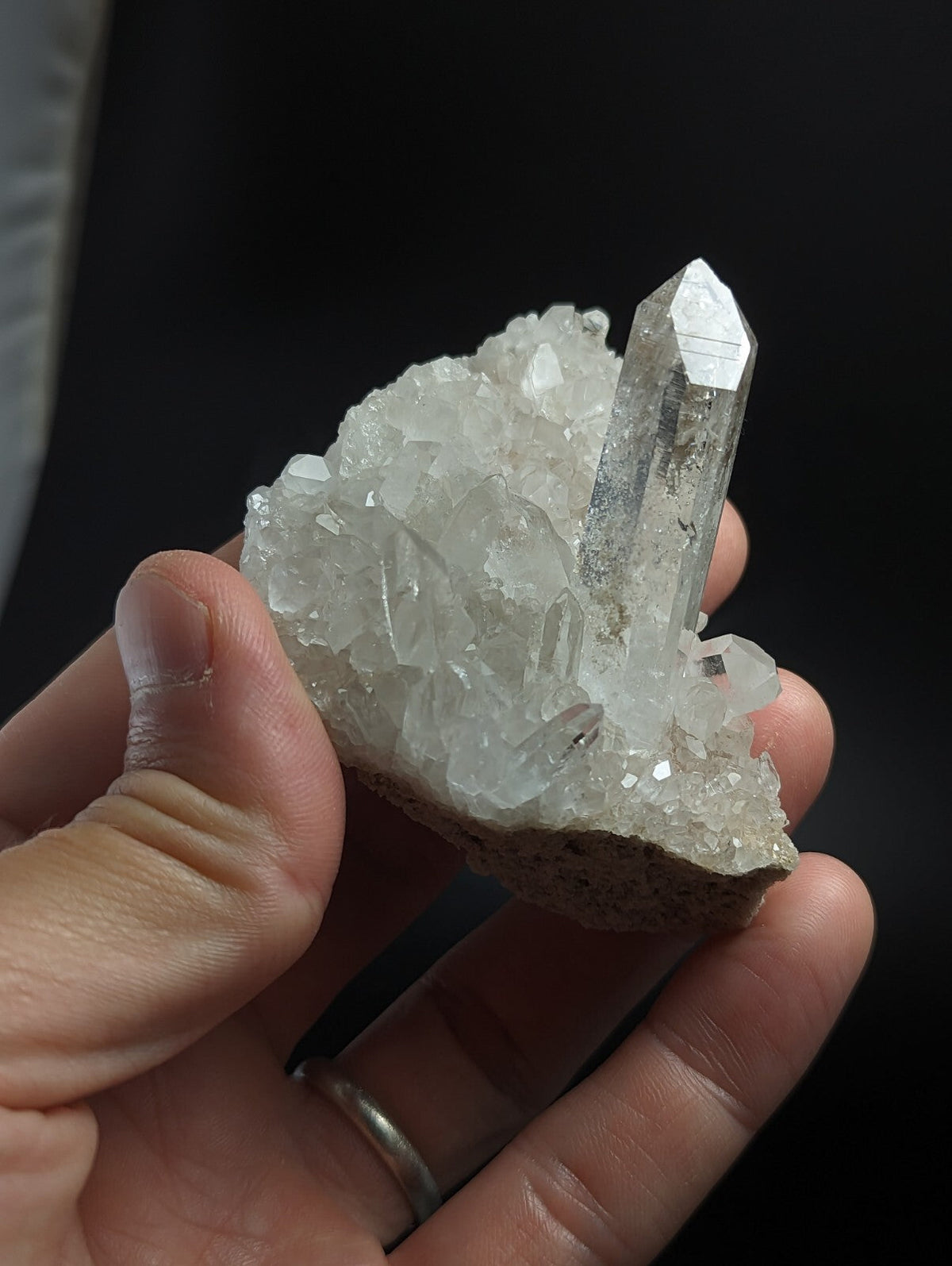 A clear, translucent quartz crystal cluster with a prominent pointed spike rising from a dense bed of smaller crystals.