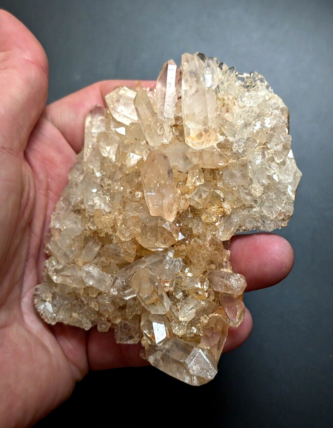 A hand holds a cluster of translucent, golden-hued quartz crystals with sharp, faceted edges and varying sizes.