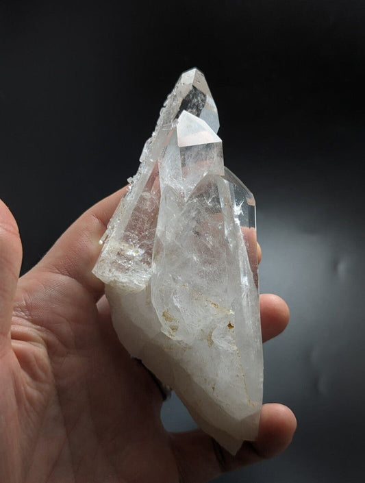 A clear, translucent quartz crystal cluster with sharp, pointed facets and a natural, rough-edged base.