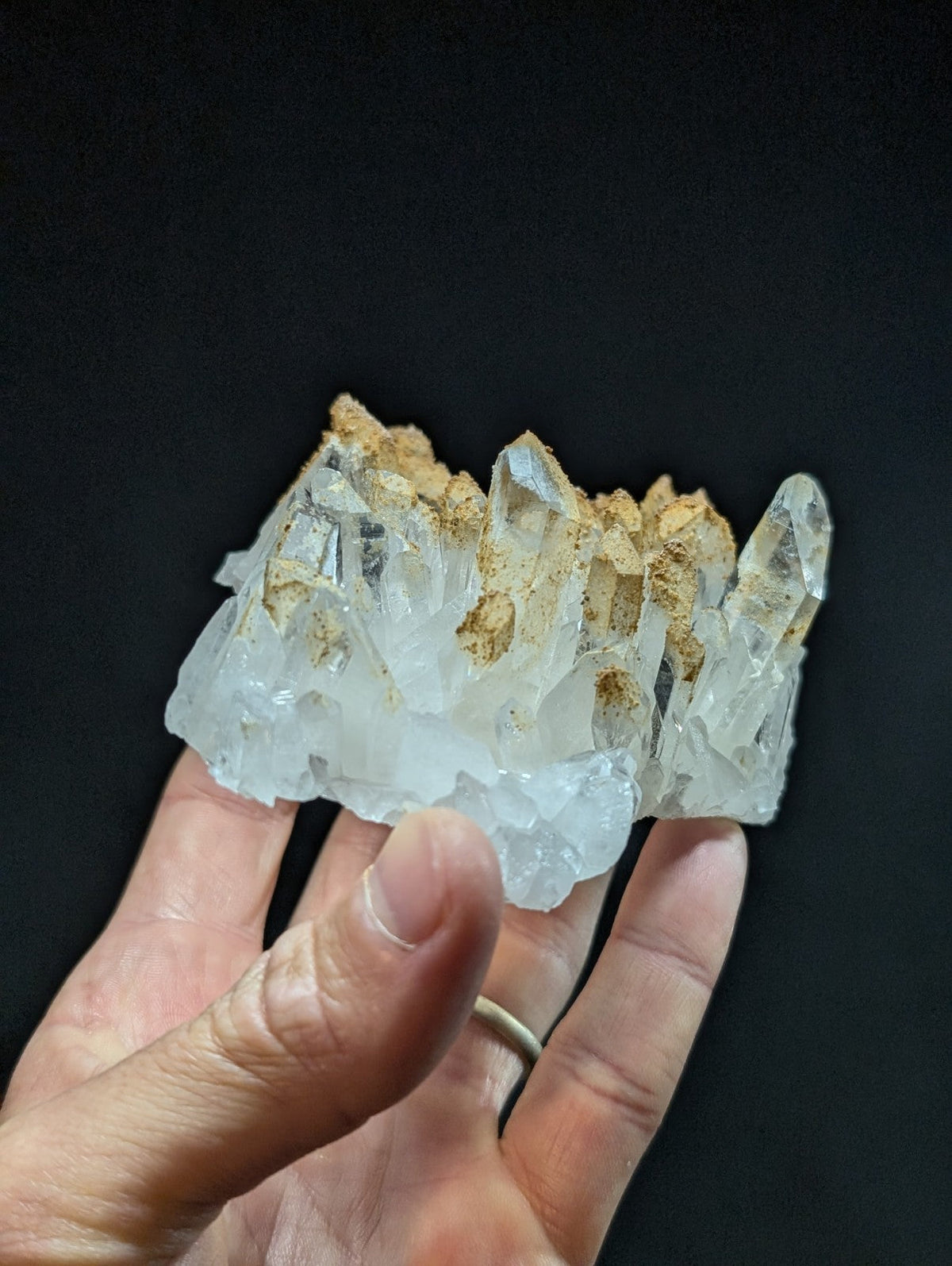 A translucent quartz crystal cluster with sharp, pointed facets and a base of earthy brown matrix material.