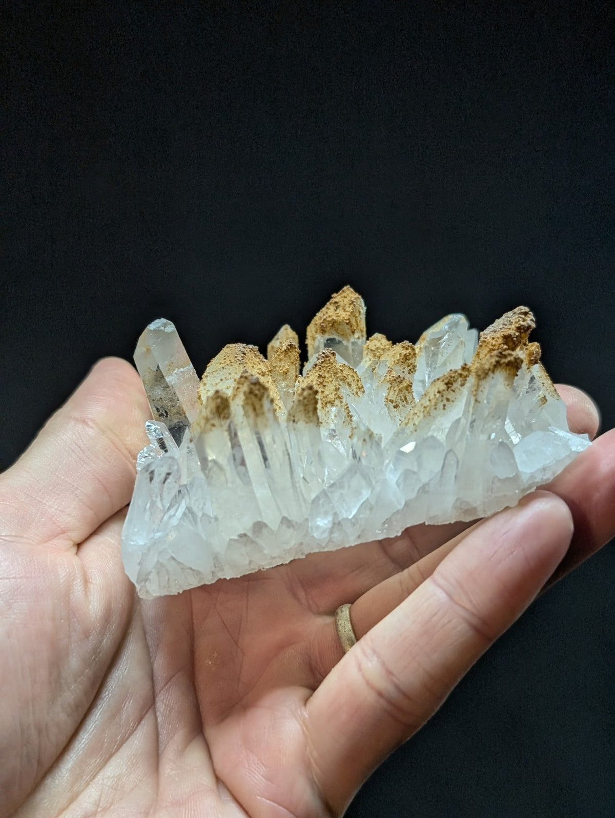 A translucent quartz crystal cluster with pointed, faceted formations and a brownish mineral cap at the top.