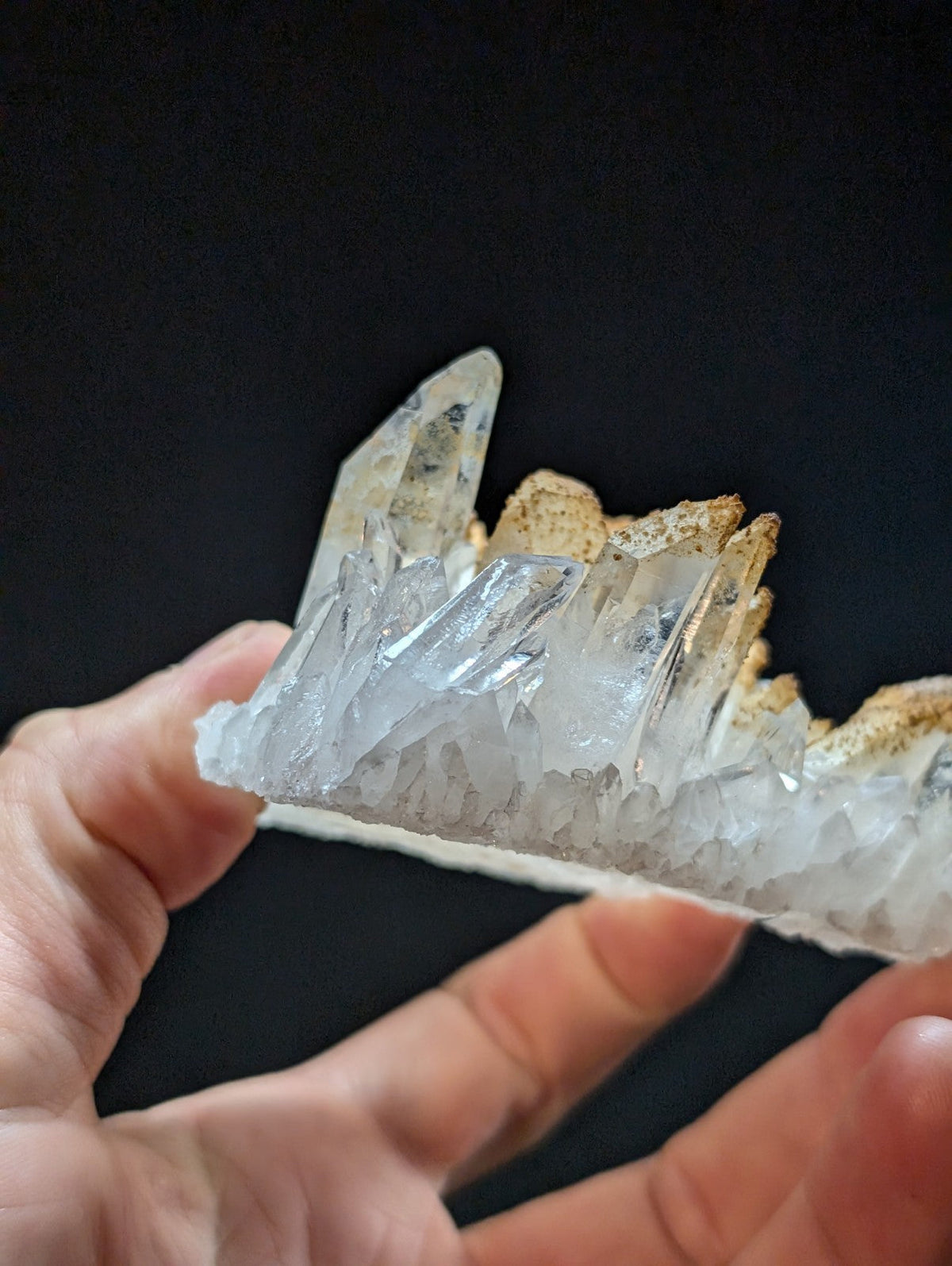 A translucent quartz crystal cluster with sharp, pointed formations and a golden-brown mineral base.