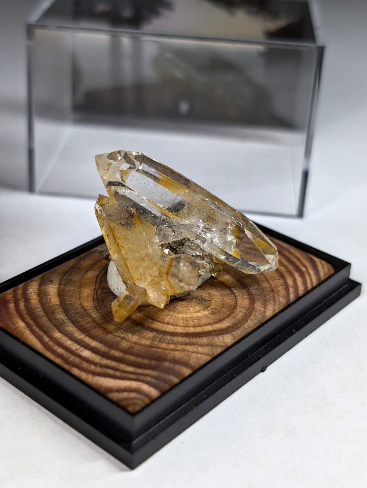A translucent yellow and clear crystal cluster displayed on a circular wood-grain base within a black frame.