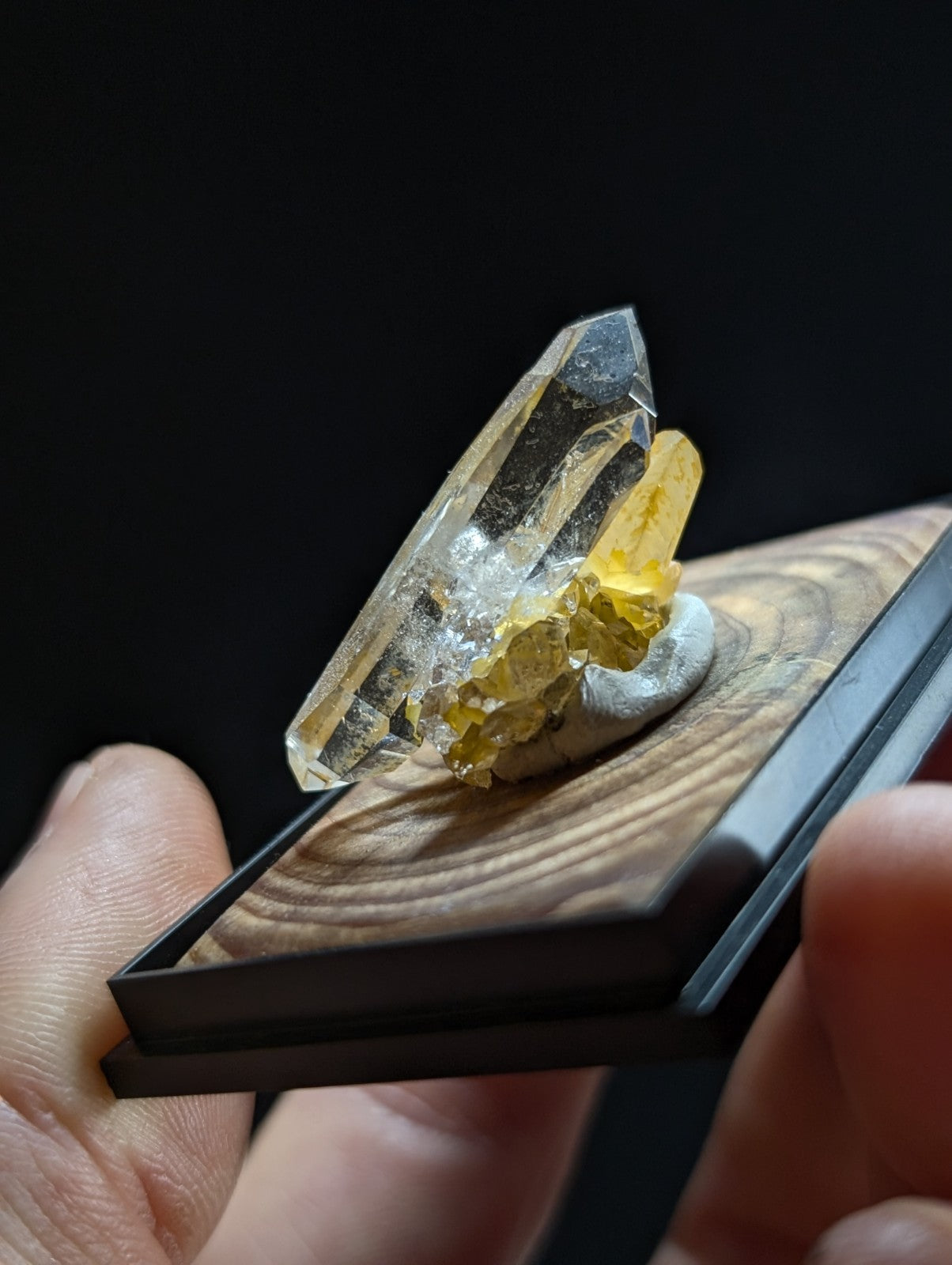 A clear, faceted quartz crystal with golden-yellow mineral inclusions rests on a wooden display base.