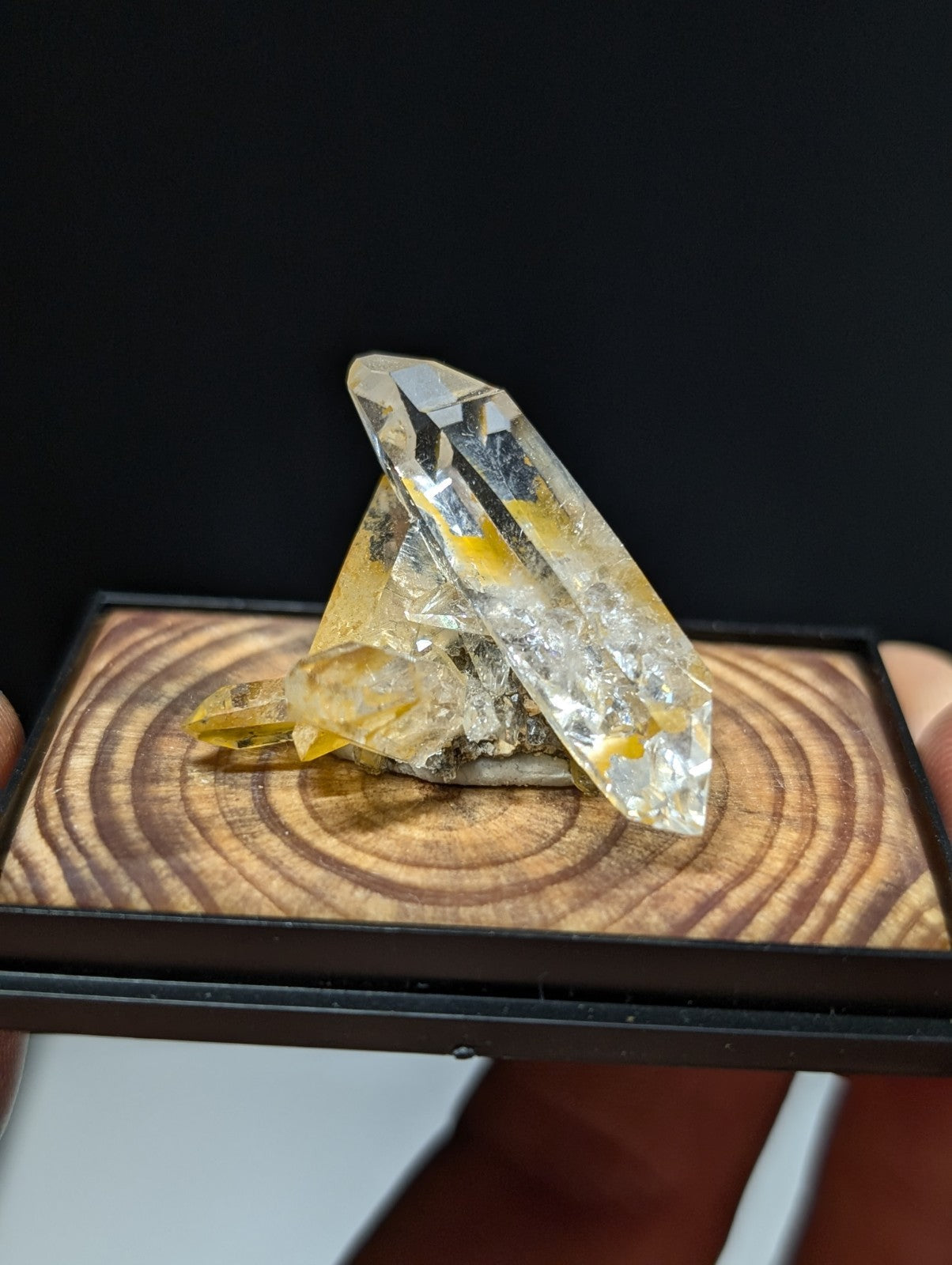 A translucent yellow and clear quartz crystal cluster with sharp, faceted points resting on a wooden display base.