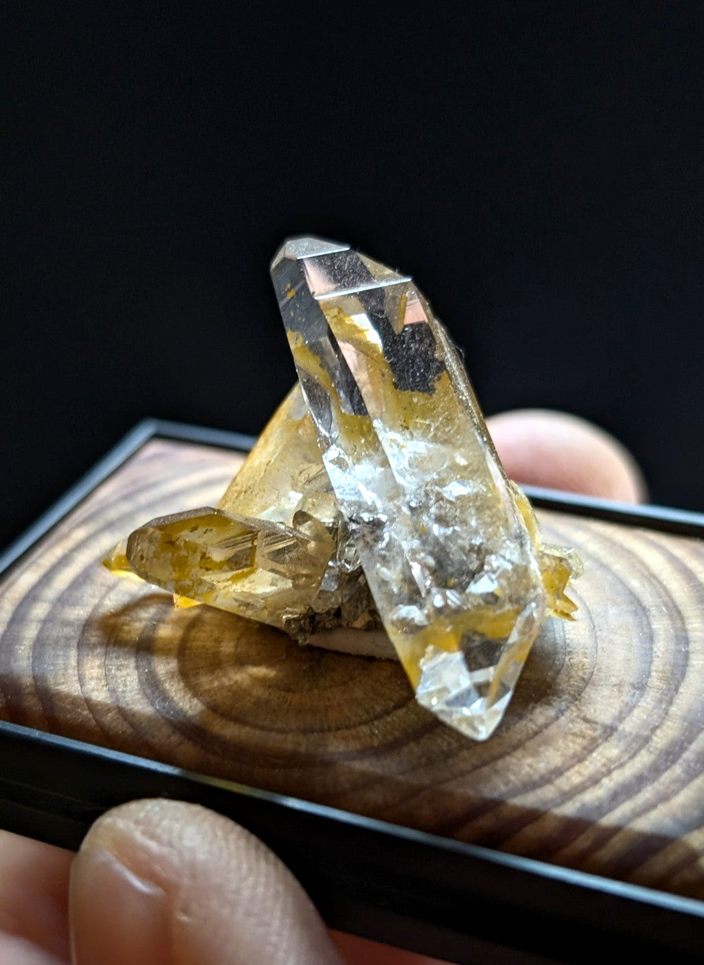 A translucent yellow crystal with clear facets and embedded dark inclusions, displayed on a wooden surface.