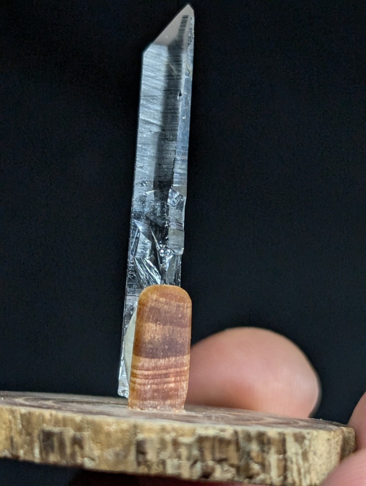 A clear, faceted quartz crystal with subtle internal striations stands upright on a wooden base.