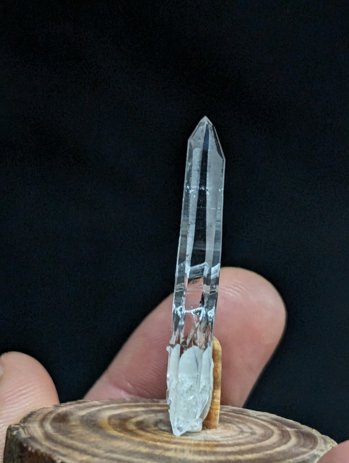 A clear, transparent quartz crystal with a pointed tip and visible internal striations stands upright on a wooden base.