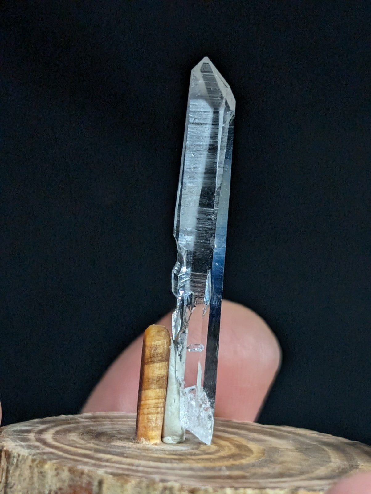 A clear quartz crystal with a pointed tip and visible internal striations, standing upright on a wooden base.