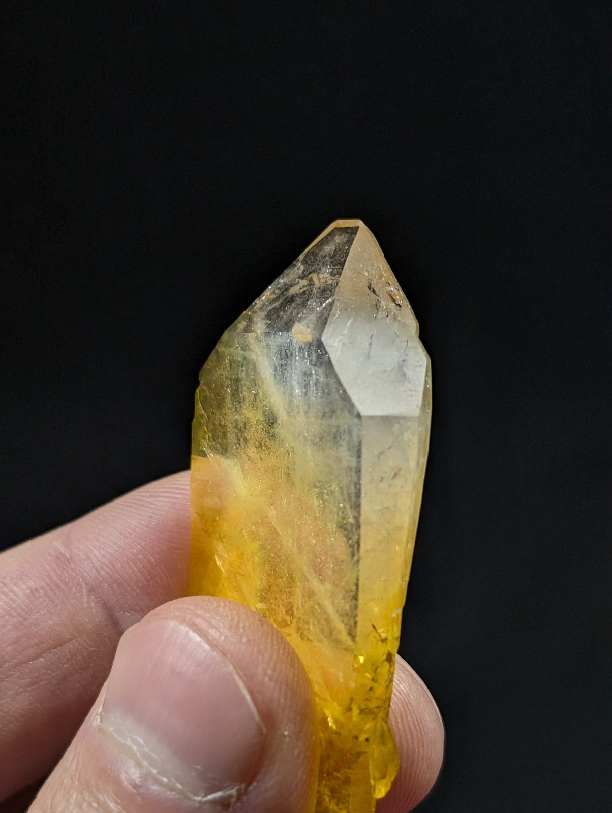 A translucent yellow crystal with a pointed tip and visible internal inclusions, held gently between fingers.