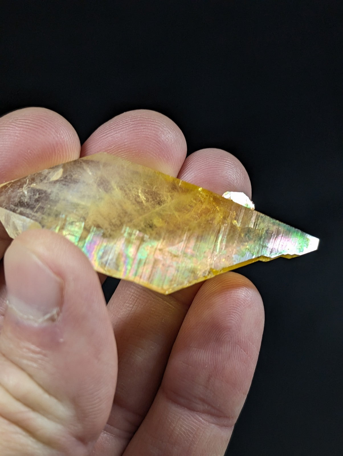 A translucent yellow crystal with iridescent rainbow reflections and sharp, angular facets.