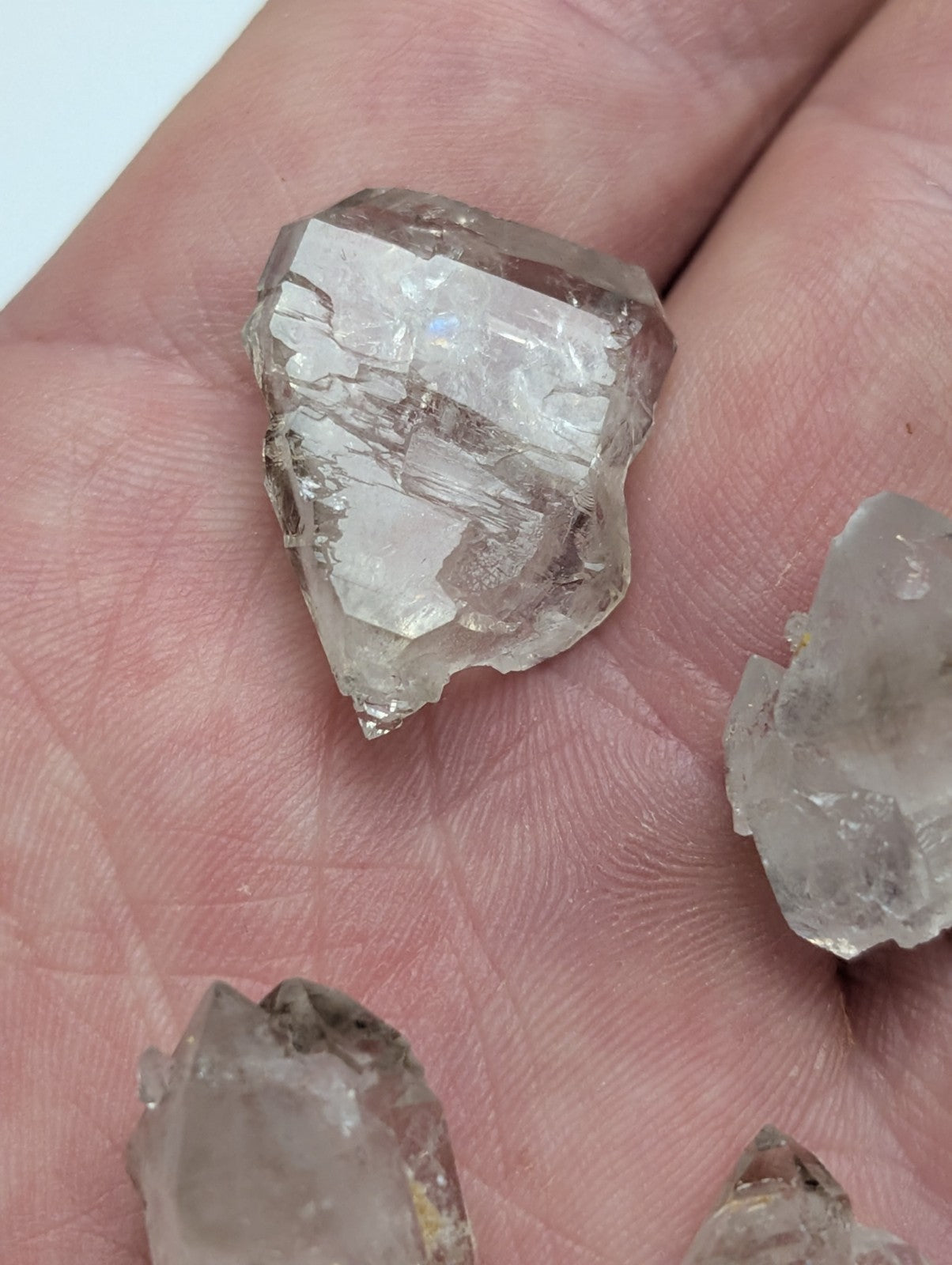 A translucent, faceted quartz crystal with a clear and slightly cloudy appearance rests in the palm of a hand.