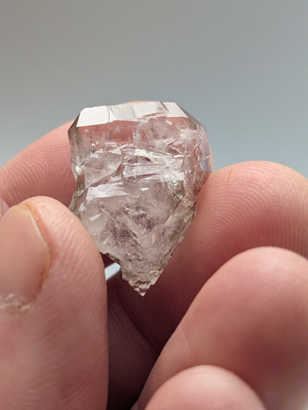 A clear, faceted quartz crystal with a rough, natural surface held gently between fingers.
