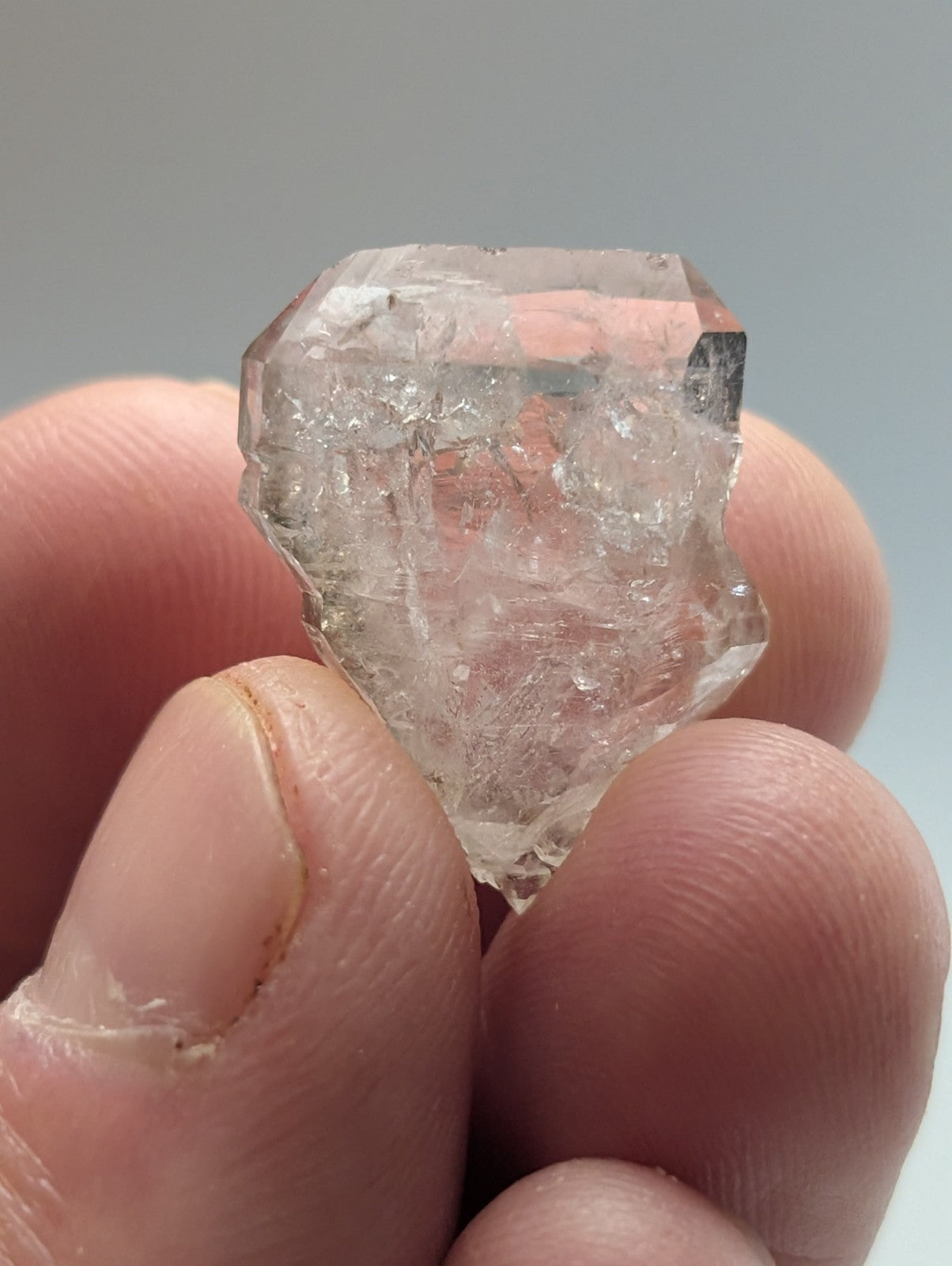 A clear, faceted quartz crystal held between fingers.