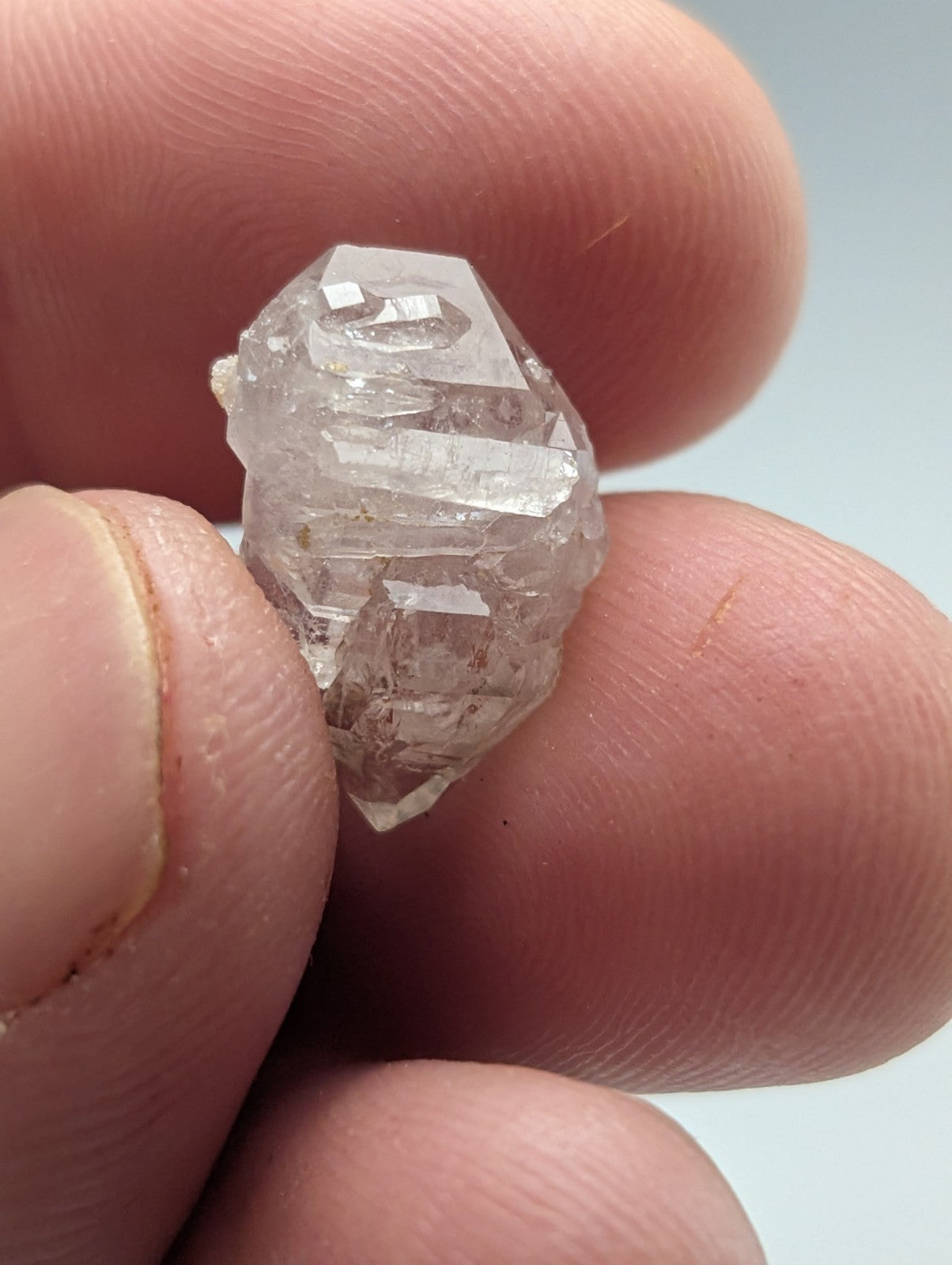 A clear, faceted quartz crystal held between fingers.