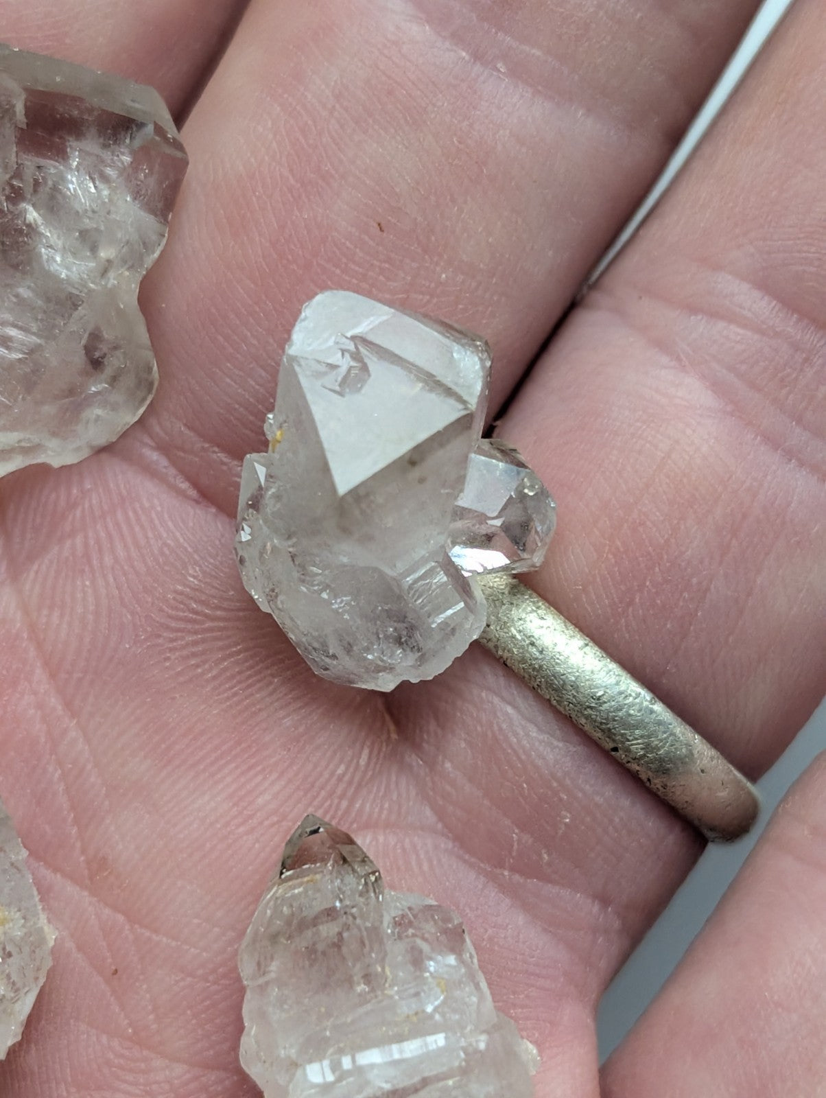 A clear, faceted quartz crystal cluster set on a rustic silver band ring.