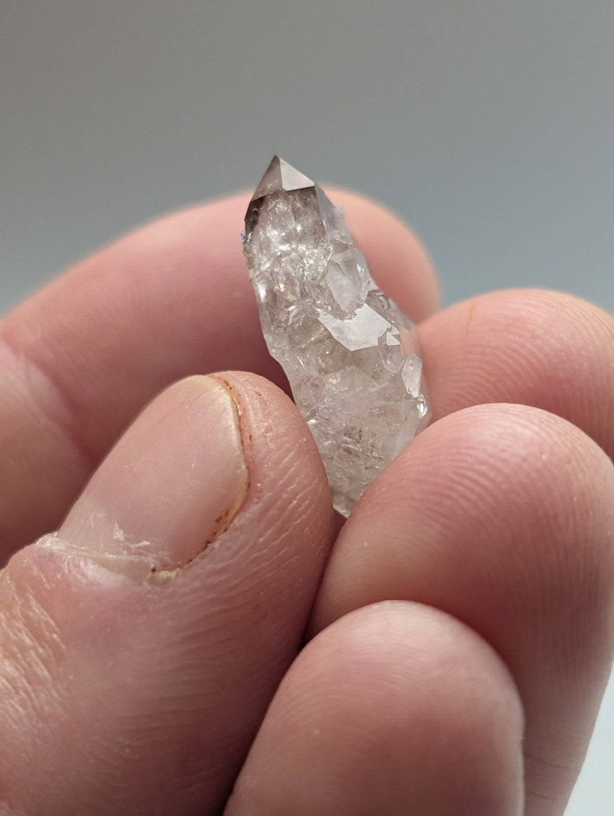 A translucent, pointed quartz crystal with a faceted tip and natural internal inclusions.
