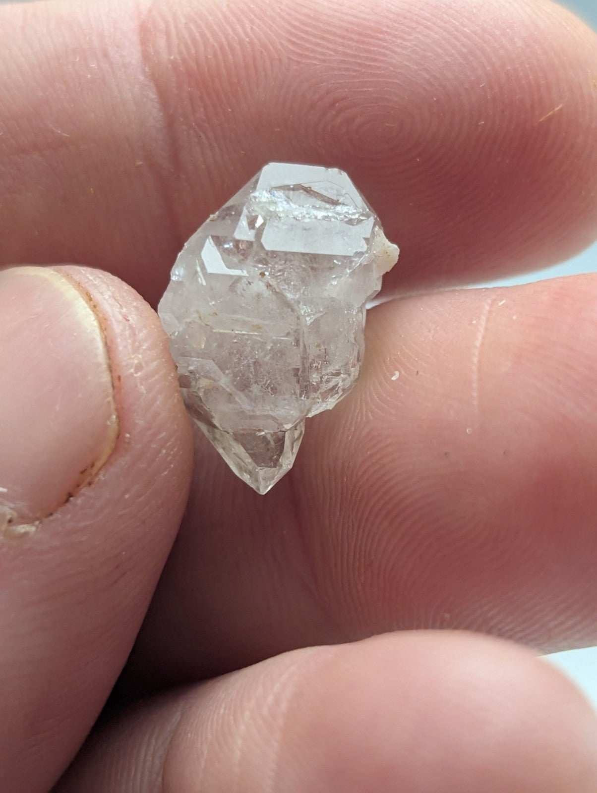 A clear, faceted quartz crystal cluster held in a hand.