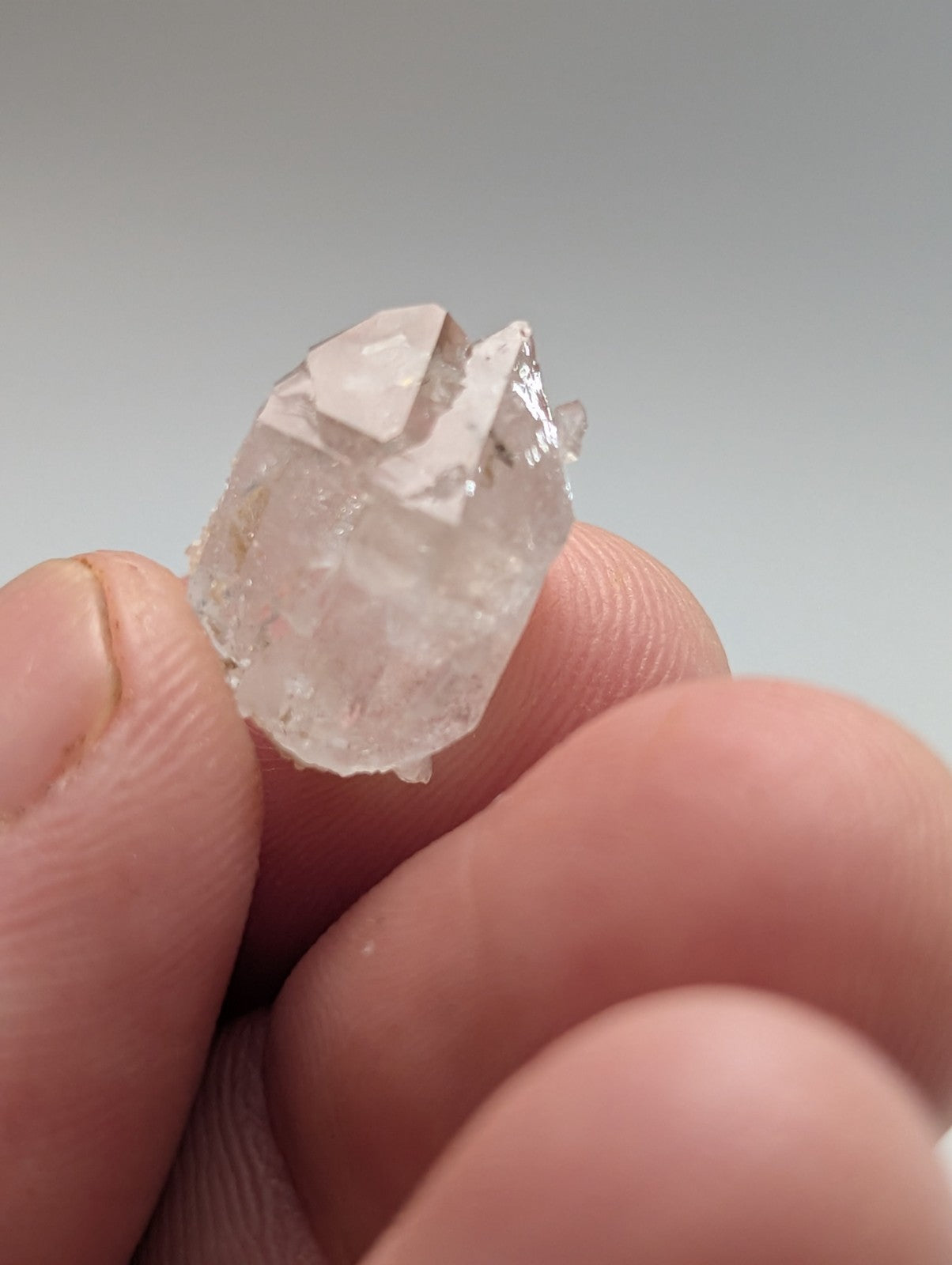 A translucent, faceted quartz crystal cluster held between fingers.