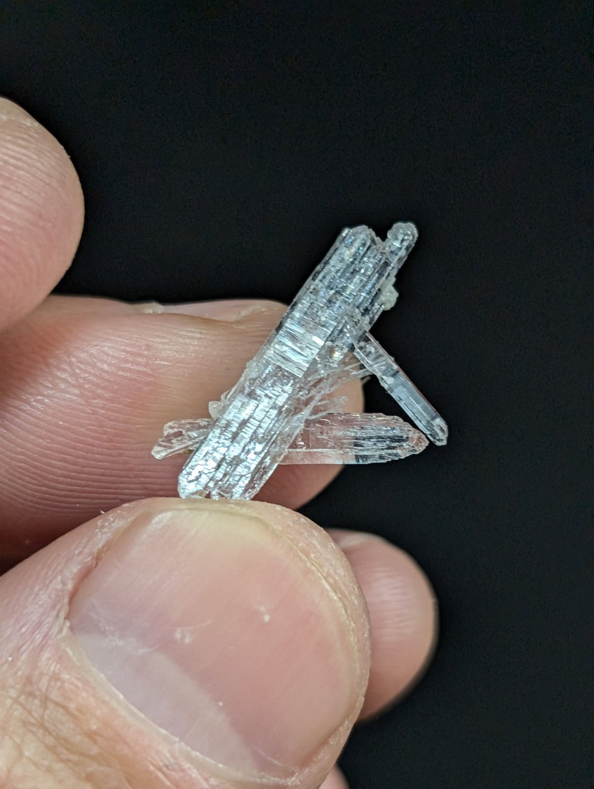 A translucent, crystalline mineral specimen with a clear, glassy appearance and distinct striations along its elongated prismatic forms.