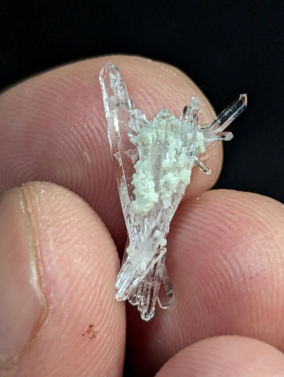 A delicate, translucent crystal cluster with clear, sharp facets and a central patch of pale greenish-white mineral growth.