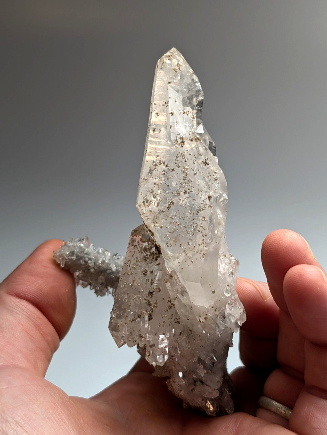 A translucent quartz crystal with dark inclusions and pointed tip held between fingers from jeffrey quarry arkansas