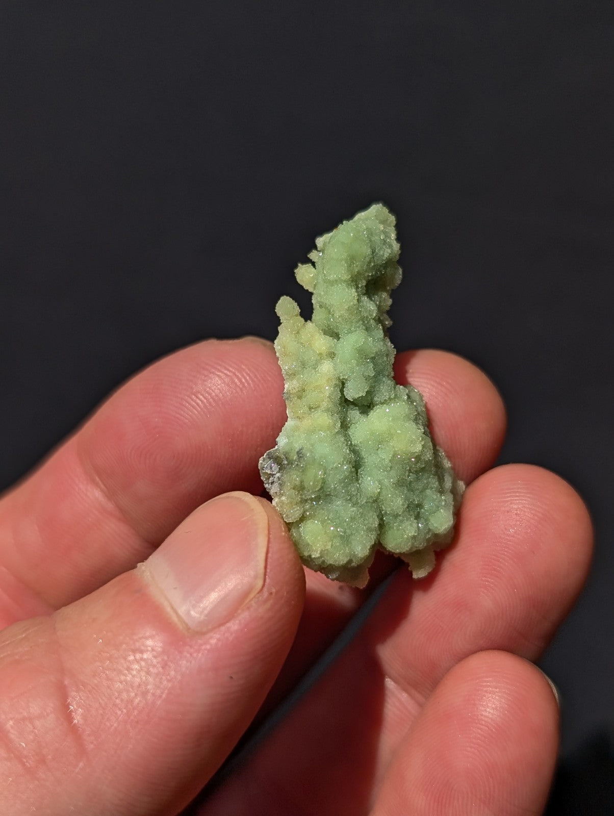 A pale green, crystalline mineral specimen with a rough, textured surface held gently in someone’s hand.