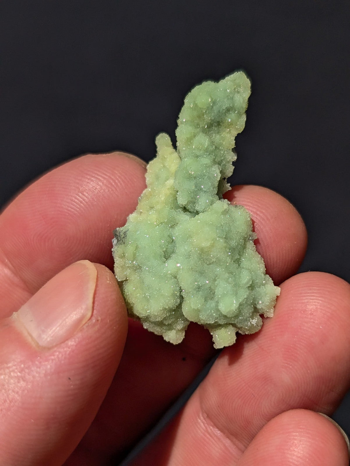 A delicate, pale green crystalline mineral specimen with a textured, faceted surface.